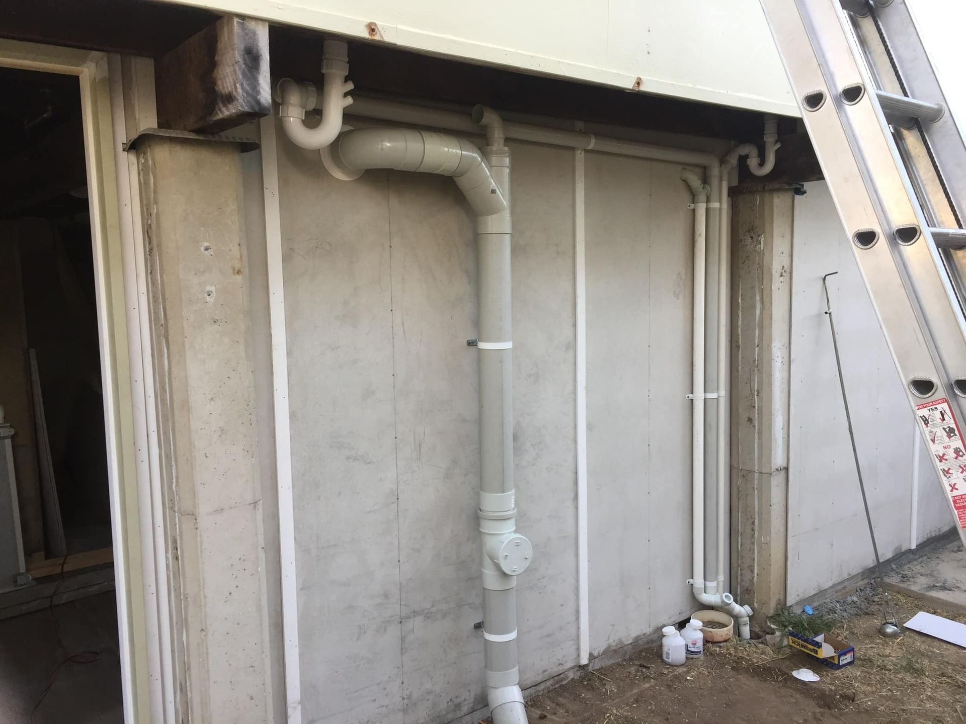 Grey Downspout on a Concrete Wall With a Ladder to the Right — Hales Plumbing & Roofing In The Range, QLD