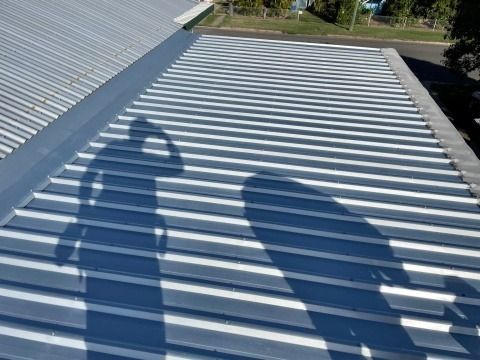 Shadow of a Person on a Ribbed, Silver Metal Roof — Hales Plumbing & Roofing In The Range, QLD