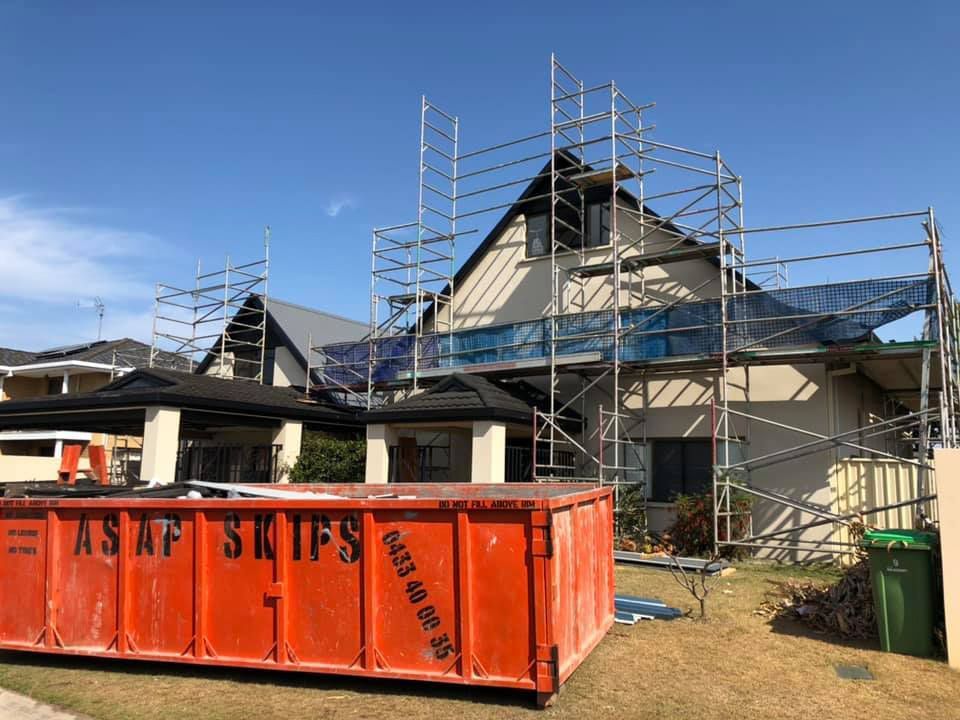 A Large Orange Dumpster Is Sitting In Front Of A House With Scaffolding Around It — Residential Roofs in Toowoomba, QLD