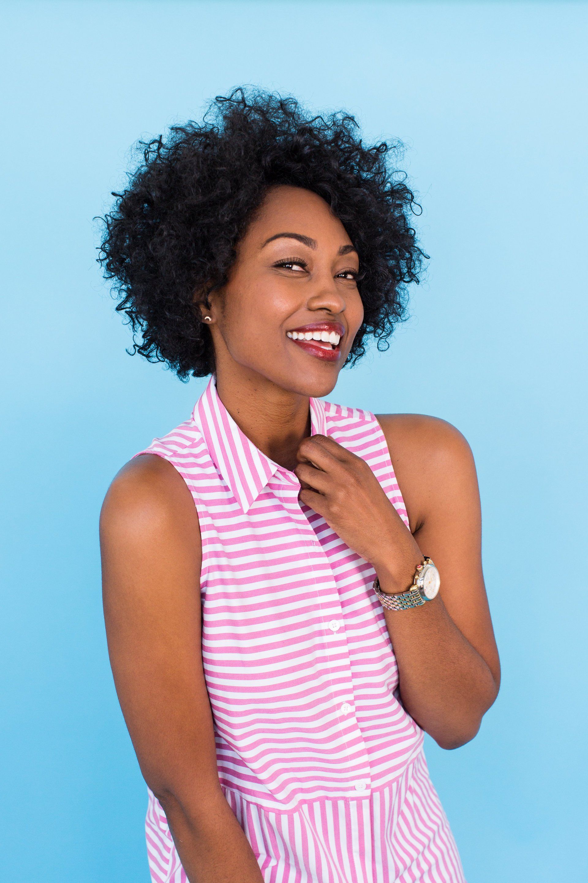 A woman in a pink and white striped shirt is smiling.