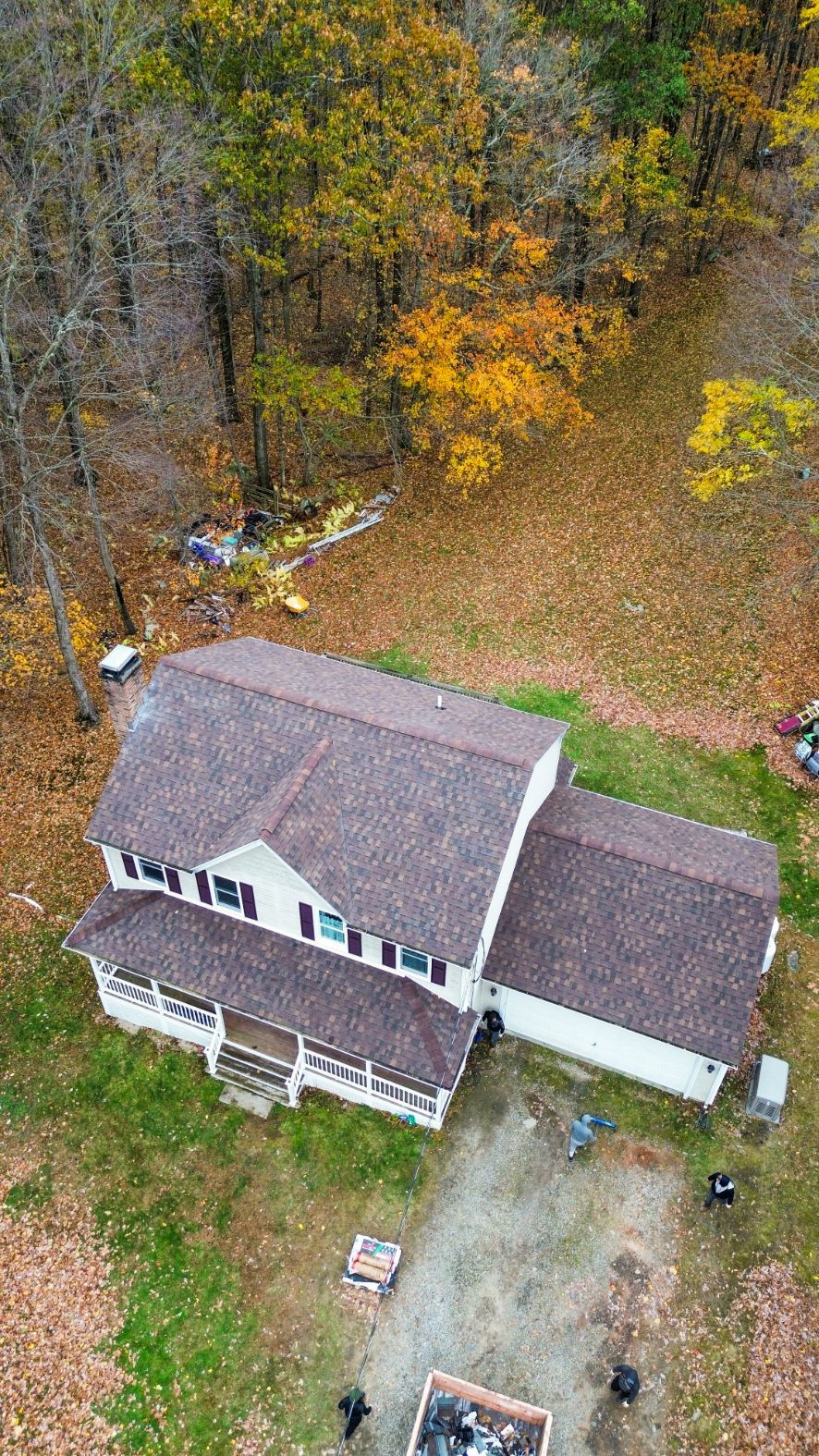 Aerial view of a gray-roofed house beside a driveway, surrounded by trees with autumn foliage.