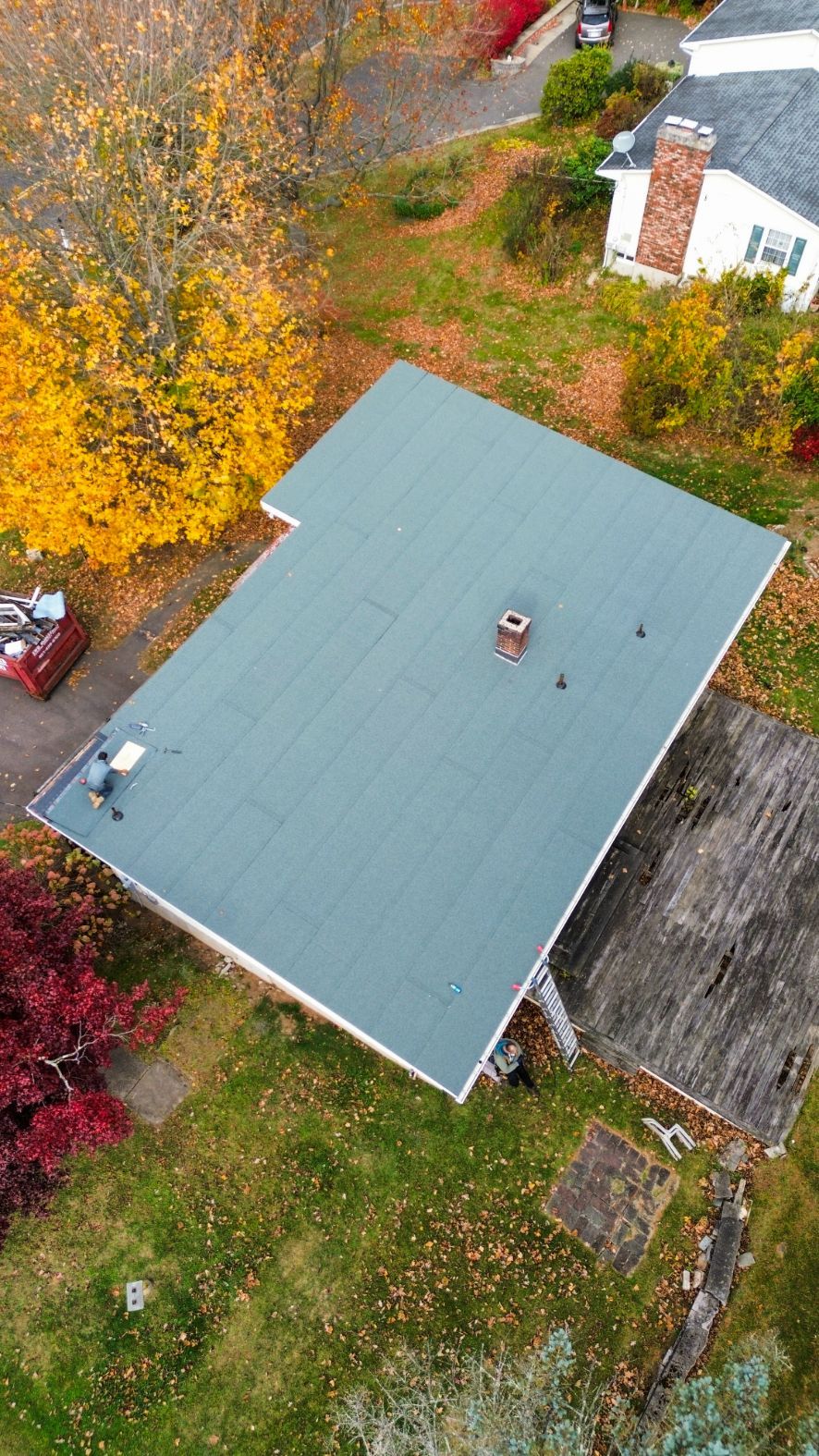Aerial view of a house with a green roof, surrounded by autumn trees and yard.
