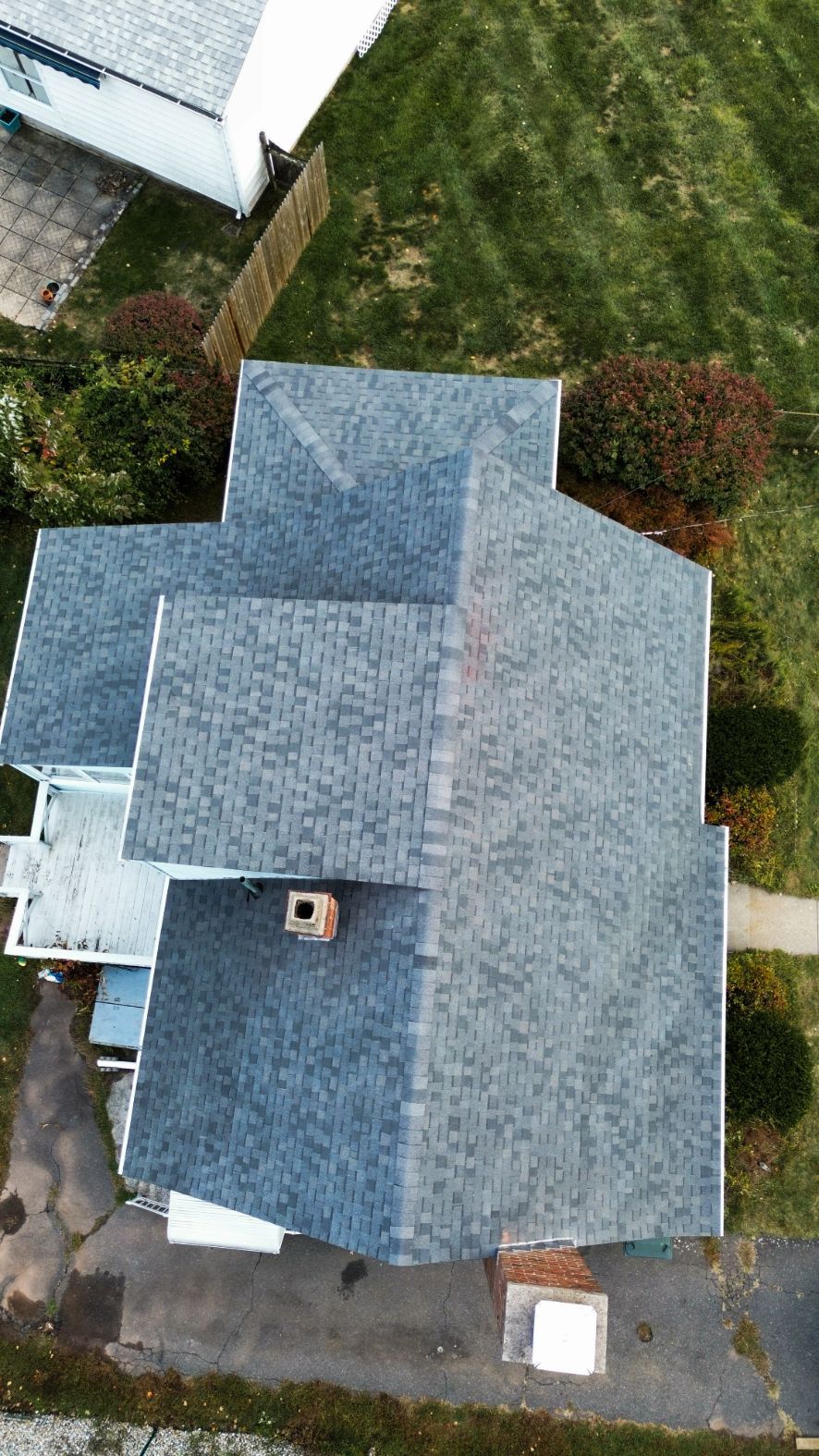 Aerial view of a gray-roofed house with a driveway and green lawn surrounding it.