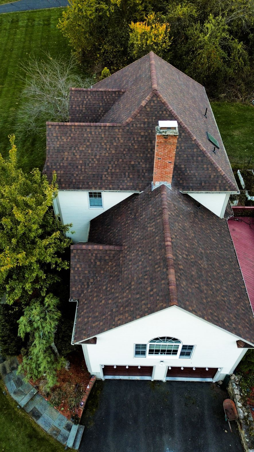 Aerial view of a white house with brown shingle roofs and a driveway, surrounded by trees.