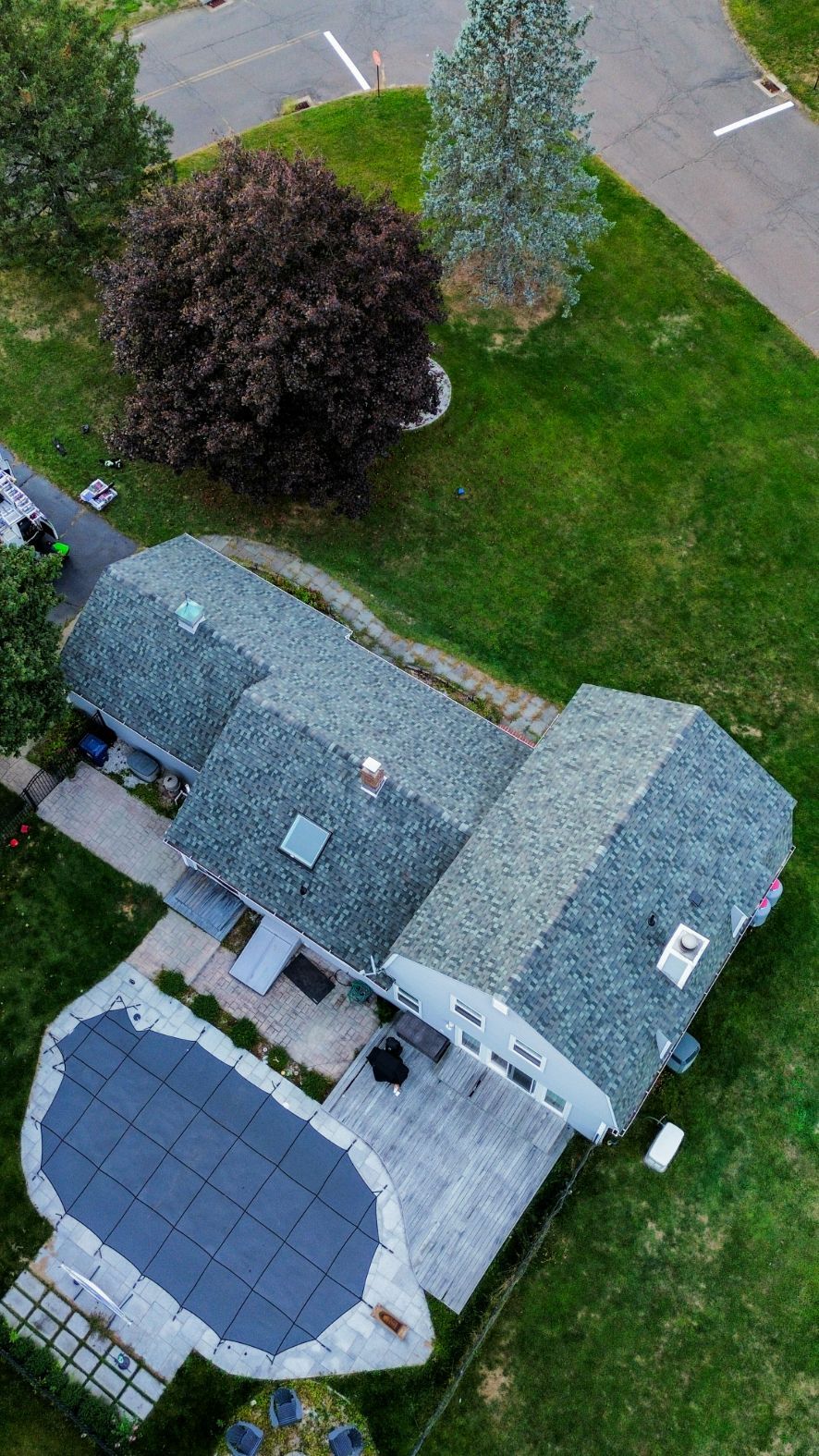Aerial view of a house with a gray roof, solar panels, lawn, and two trees by the driveway.