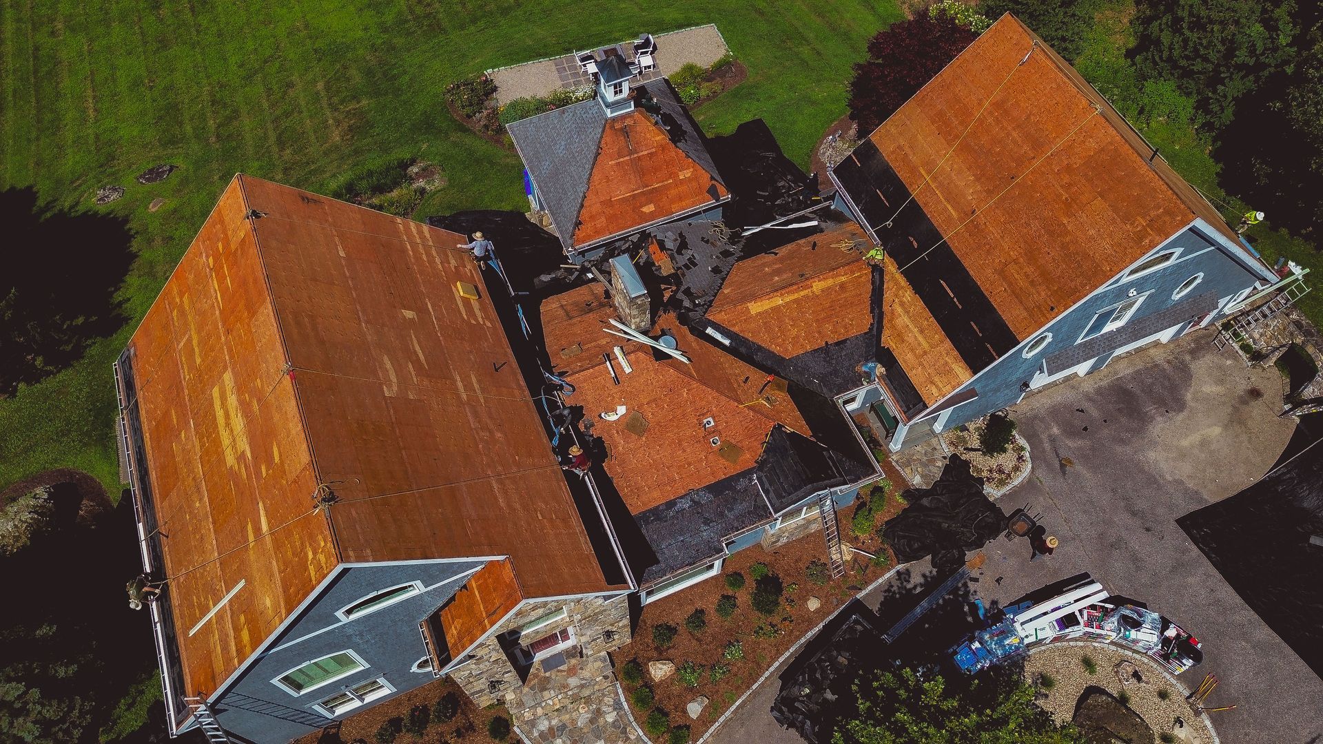 Overhead view of a house with orange-brown roofs, surrounded by green grass and a dark gray driveway.