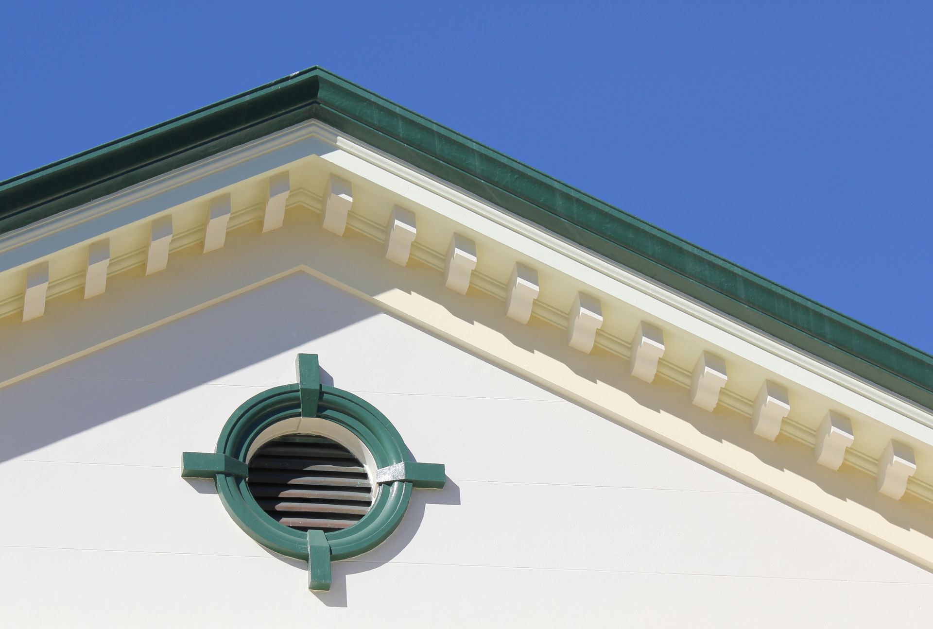 Green and white building corner with a round vent and blue sky.