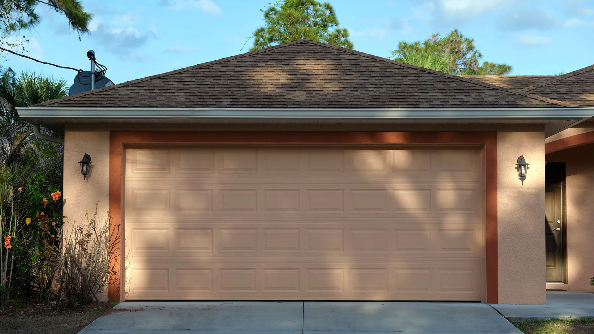 Tan garage door on a peach-colored house with a brown roof; sconces flank the door.