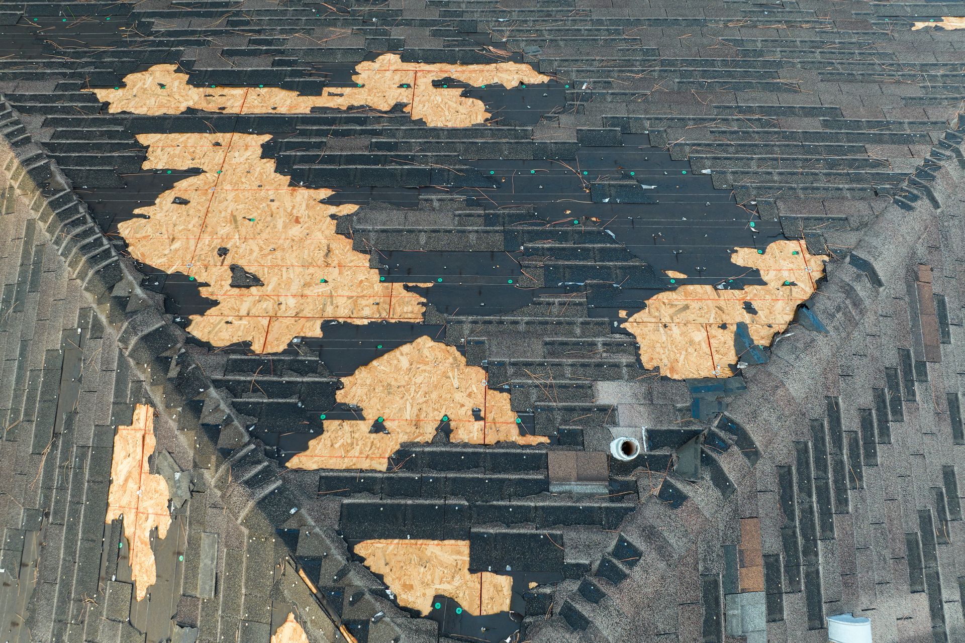 Damaged asphalt shingle roof, with missing shingles exposing wood.