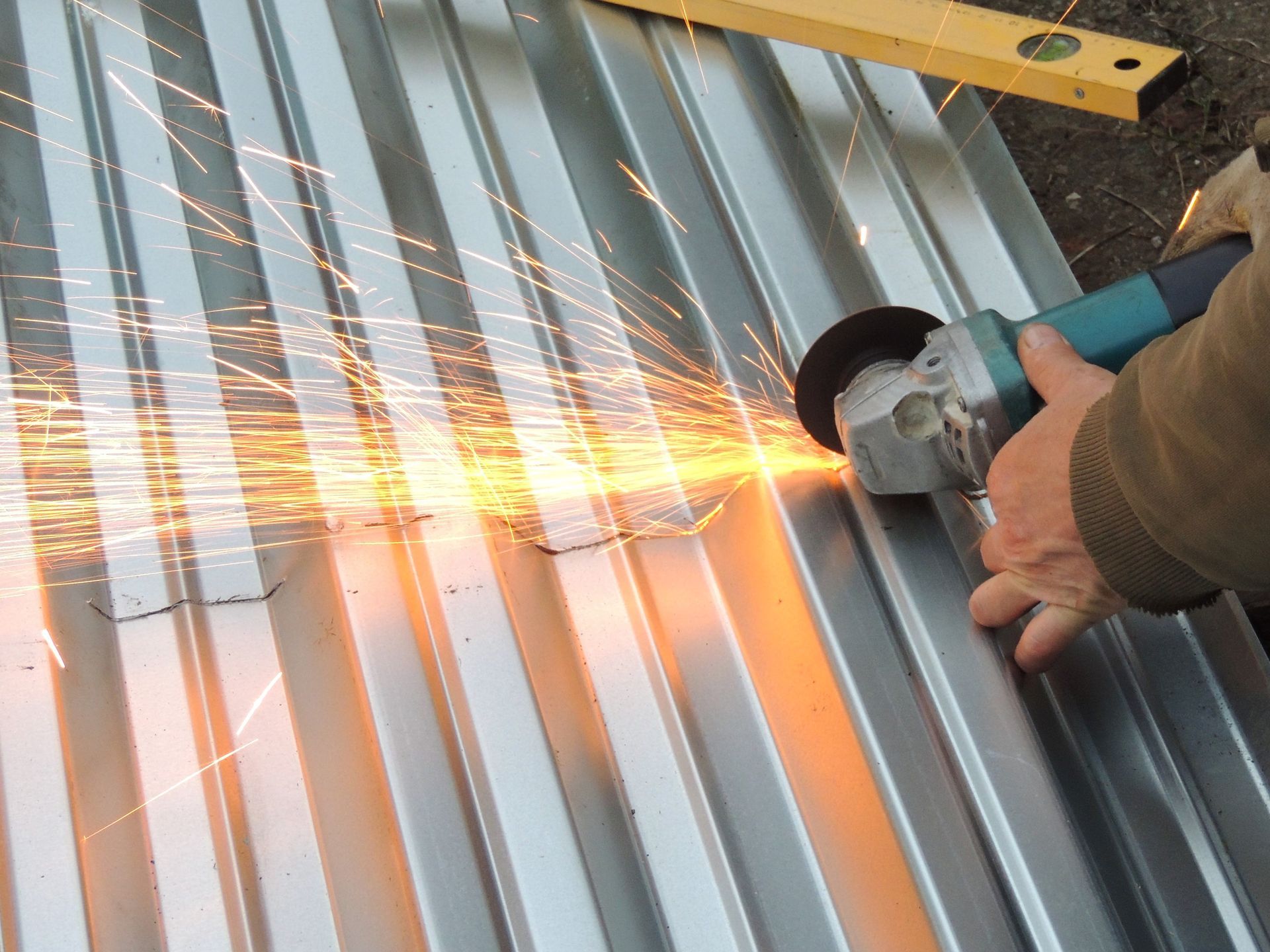 Person using an angle grinder on corrugated metal, creating sparks.