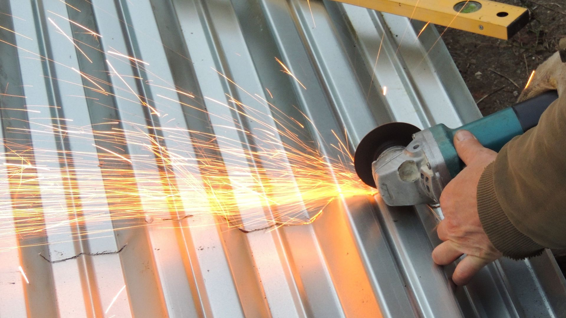 Person using a grinder to cut metal sheet, creating sparks outdoors.