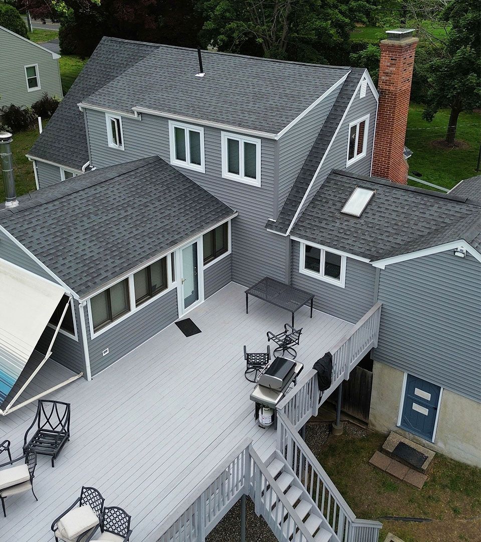 Gray house with a deck, chairs, and a grill. A pool is partially visible on the left.