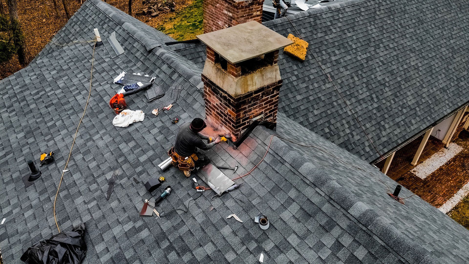 A man is sitting on top of a roof working on a chimney.