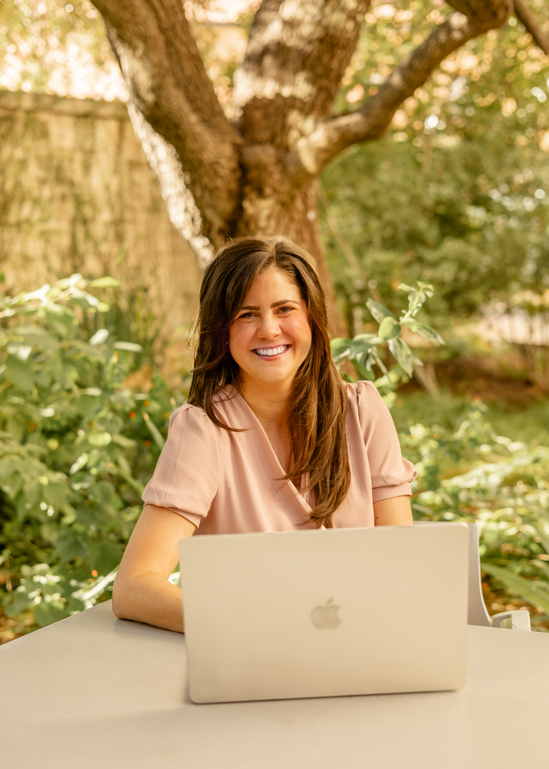 A woman is sitting at a desk with a laptop and a vase of flowers.
