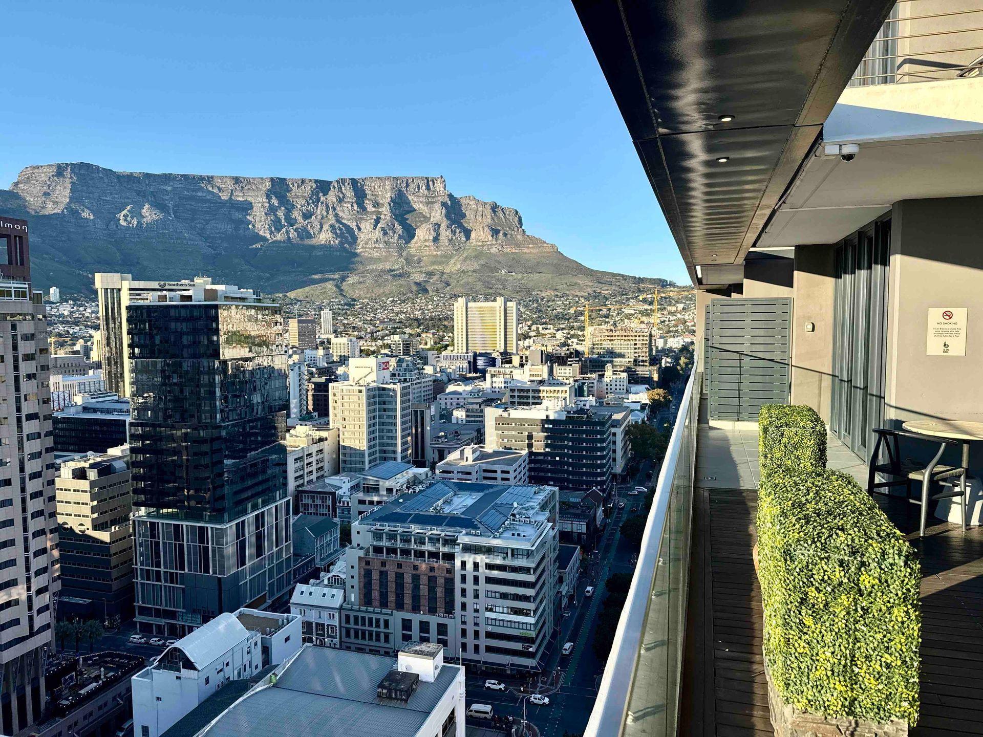 City skyline with a mountain backdrop viewed from a balcony in bright daylight.