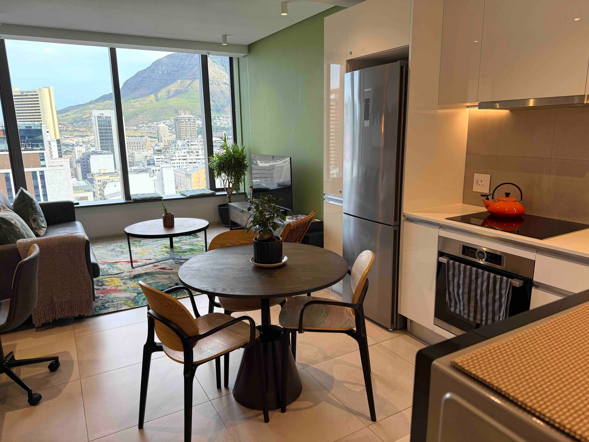 Modern apartment living room and kitchen with large windows, mountain view, and round dining table