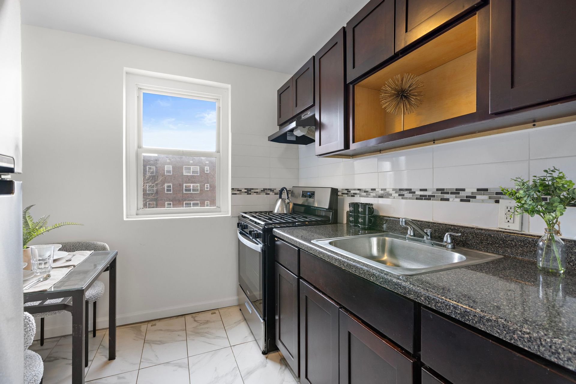 A kitchen with a stove , sink , cabinets and a window.