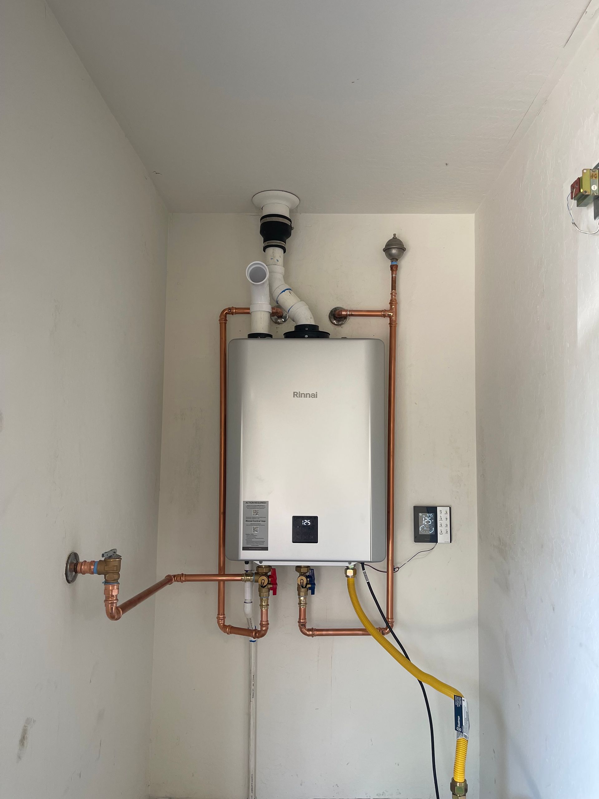 Tankless water heater with copper pipes in a white-walled utility closet.