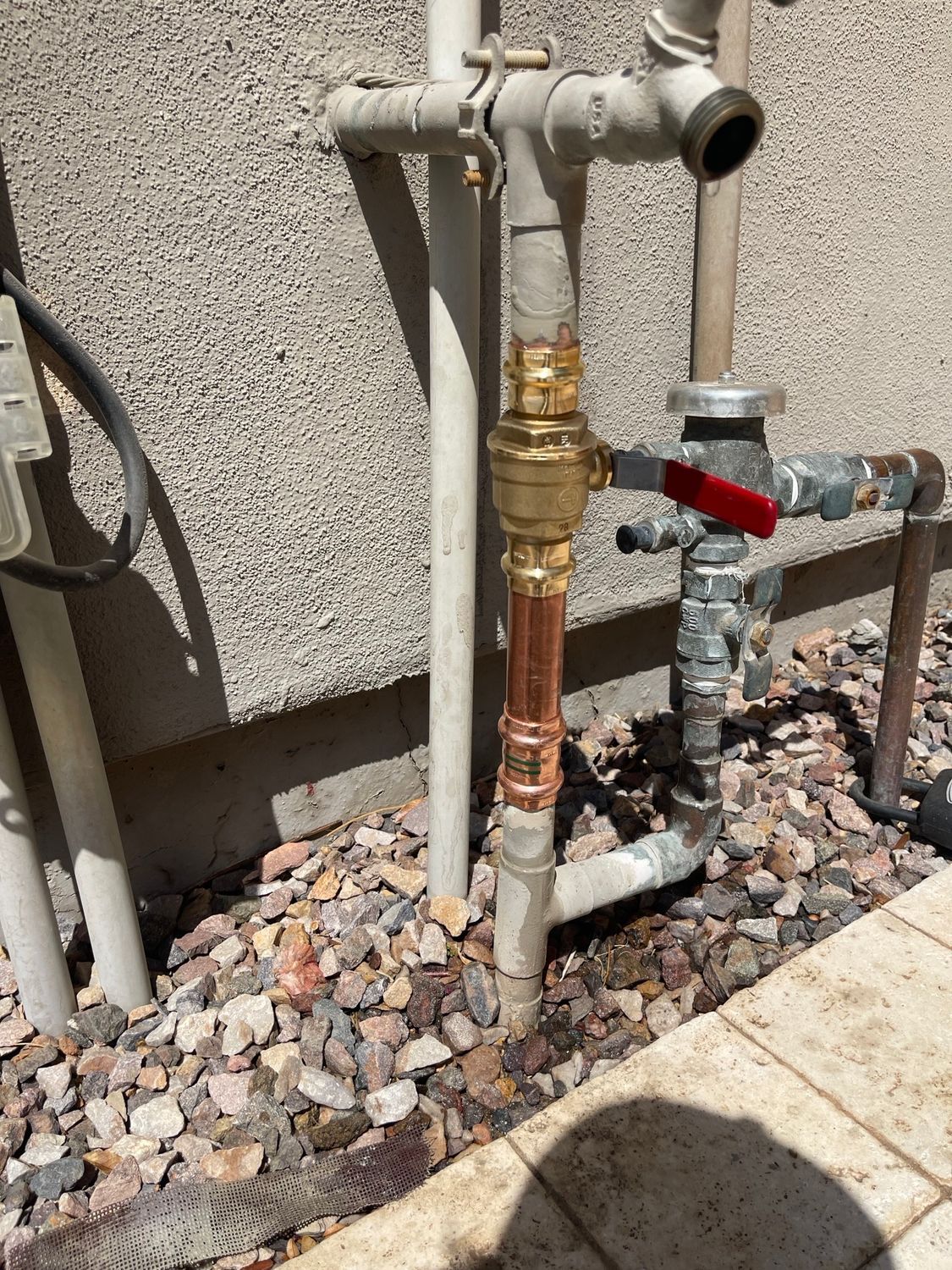 Plumbing pipes: copper, brass, and galvanized steel, connected to a gas line with a red valve.