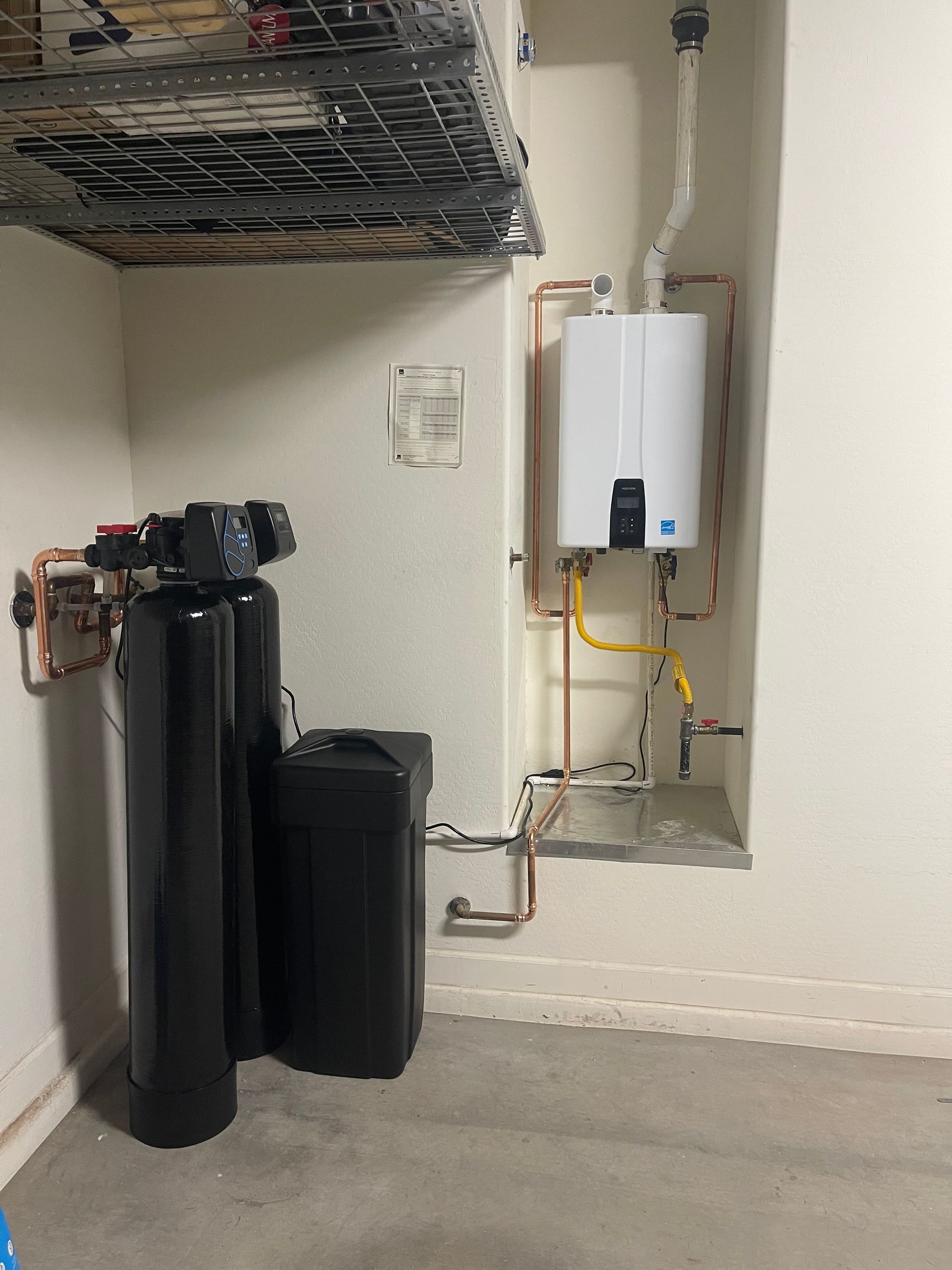 Water heater in a garage, next to a water softener and expansion tank; copper pipes visible.