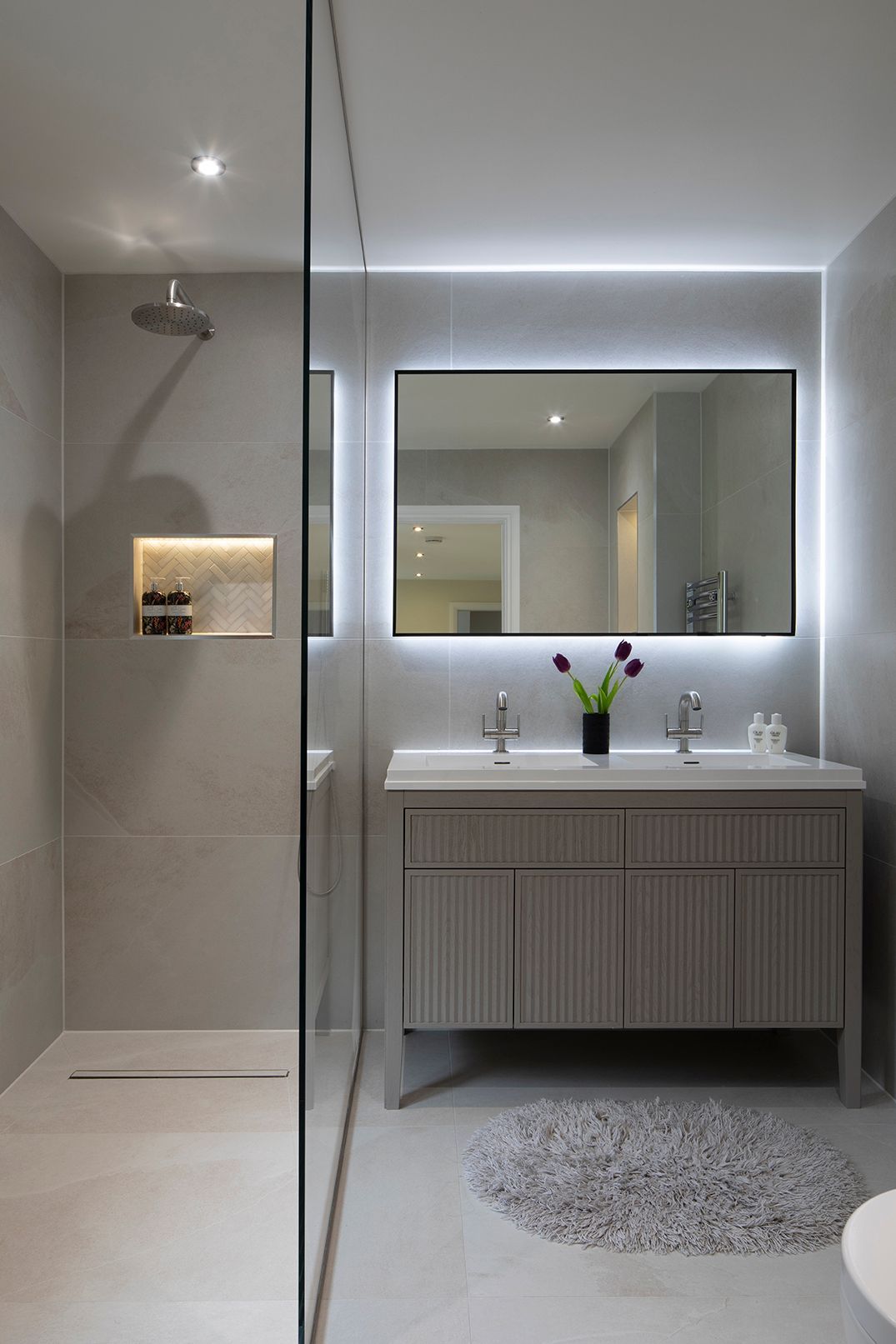 Spa-inspired bathroom with LED-backlit mirror, walk-in shower, and herringbone niche in Tewin by Elisa Design
