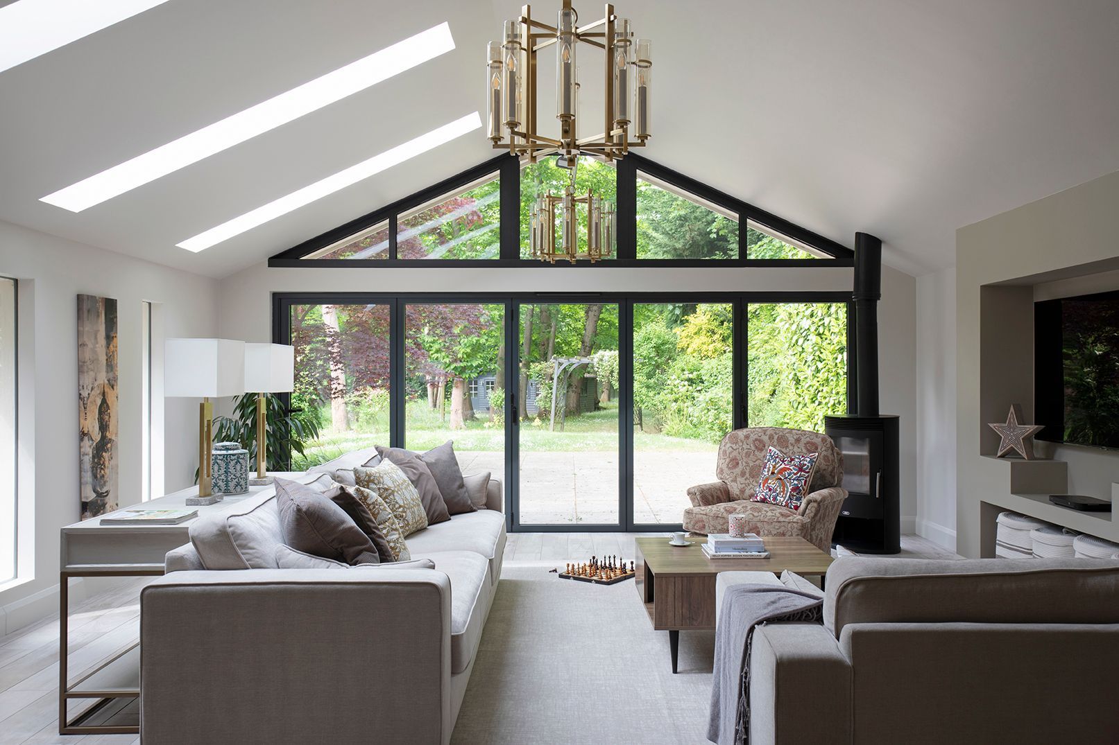 Modern heritage living room with vaulted ceiling, large black‑framed glazing and neutral sofas overlooking a leafy garden.