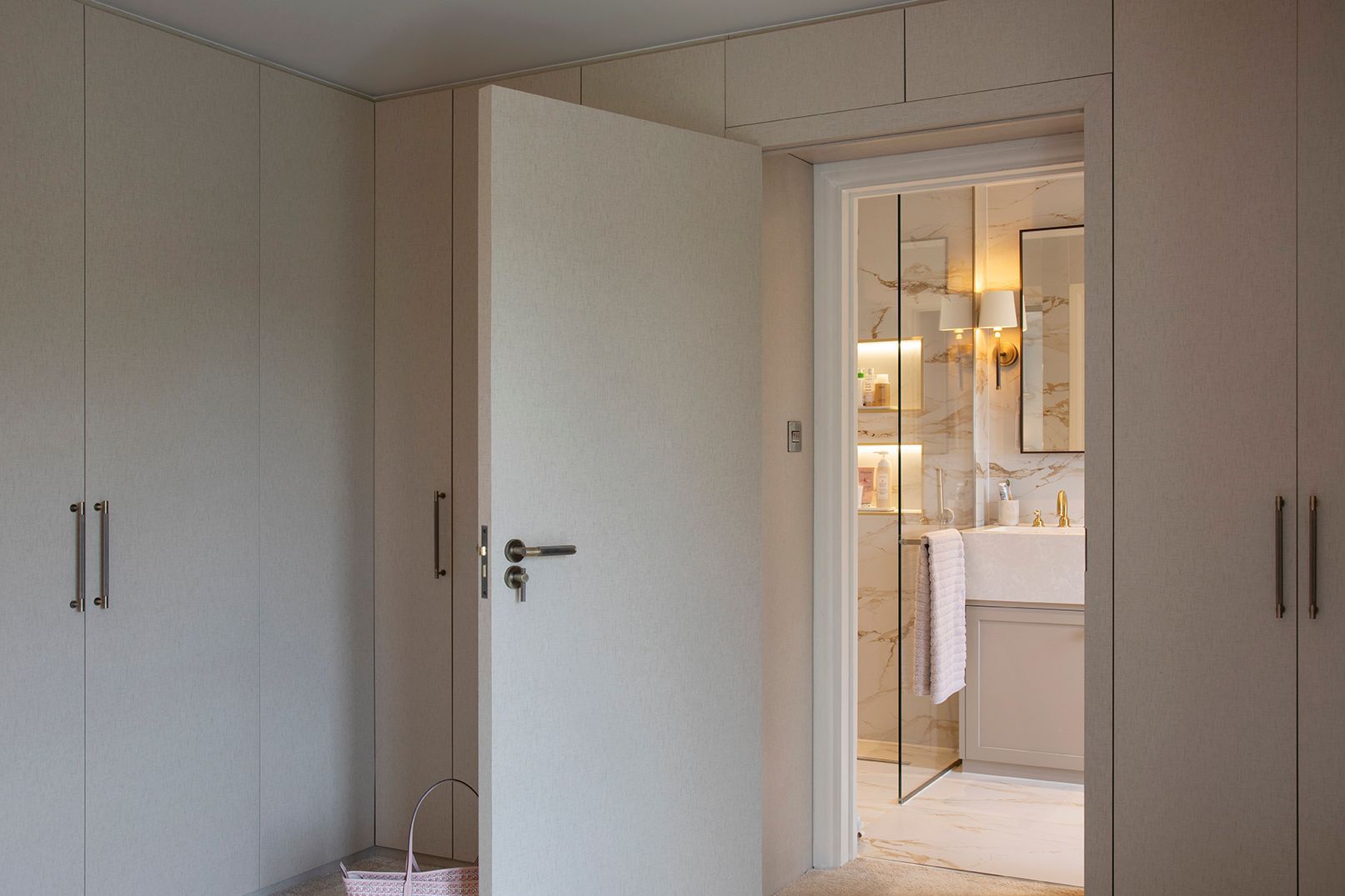Floor-to-ceiling bespoke wardrobes with view through to marble ensuite in Hertford master bedroom by Elisa Design