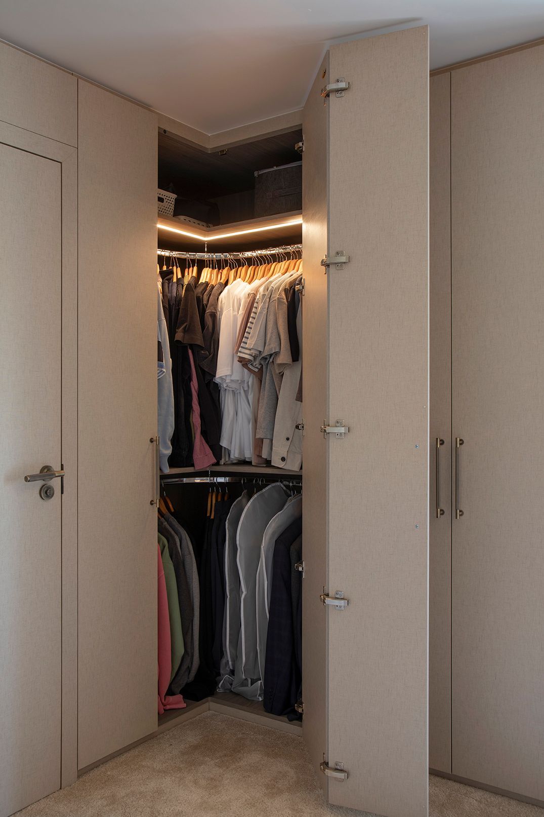 Interior of bespoke corner wardrobe with integrated LED lighting, hanging rail, and upper shelf storage in Hertford bedroom