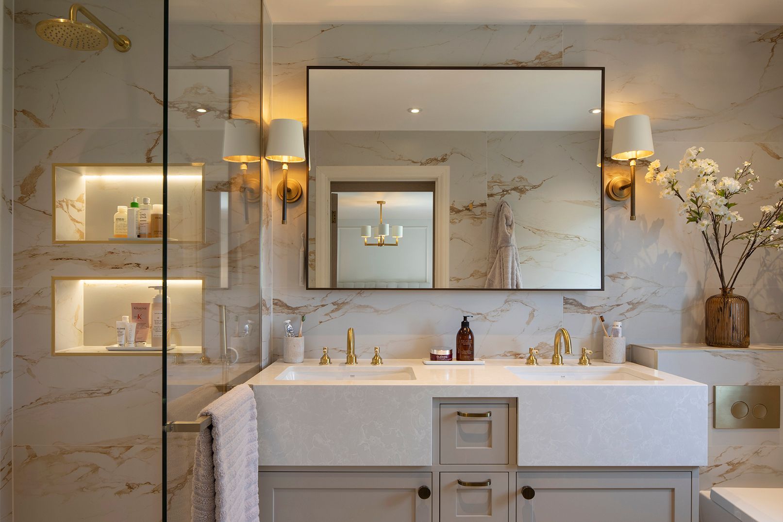 Luxury ensuite with marble-effect tiles, double vanity, brass fixtures, and LED-lit shower niches in Hertford by Elisa Design