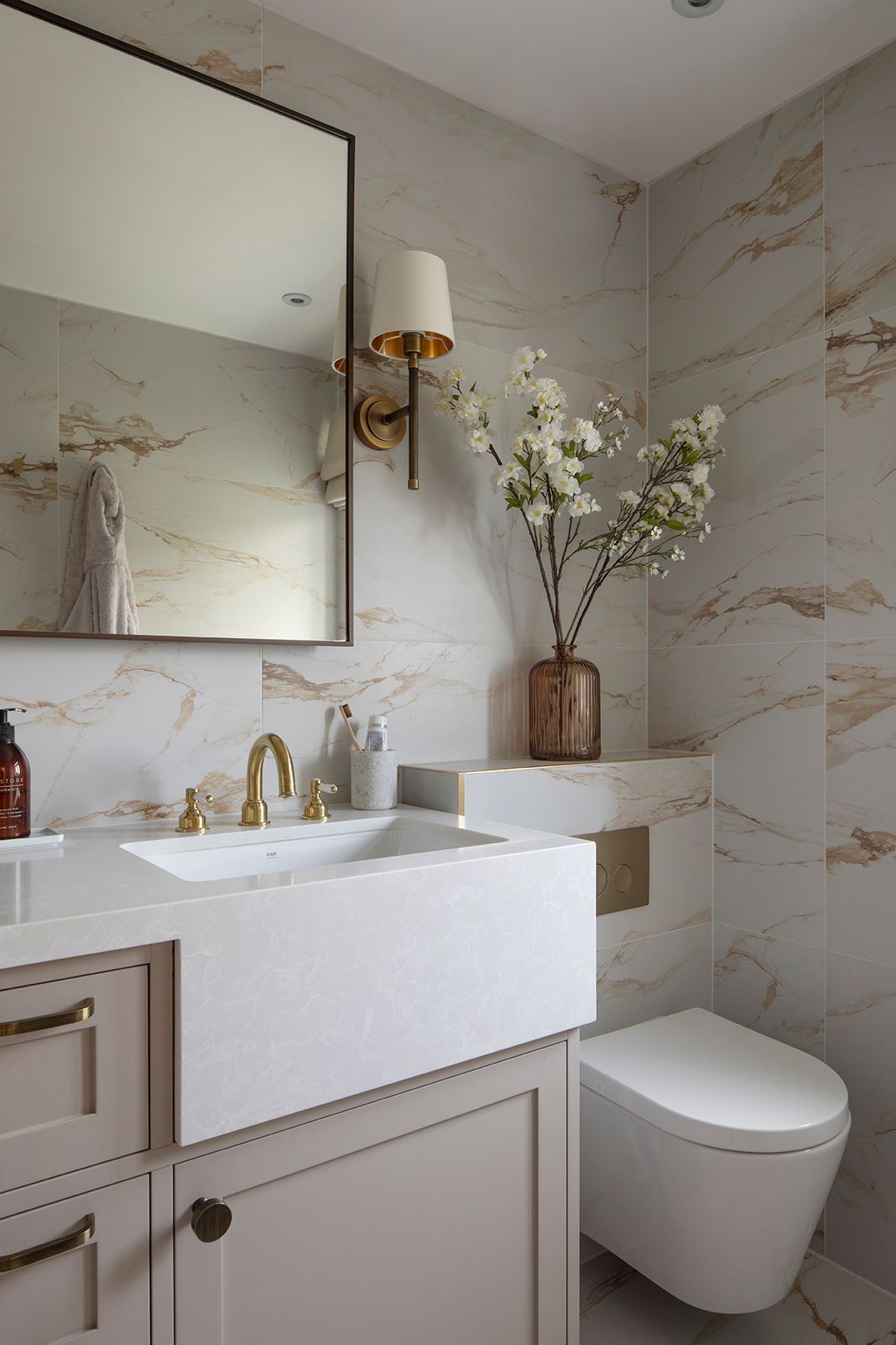 Marble-effect ensuite detail with brass three-hole taps, white flowers, and wall-hung toilet in Hertford bathroom