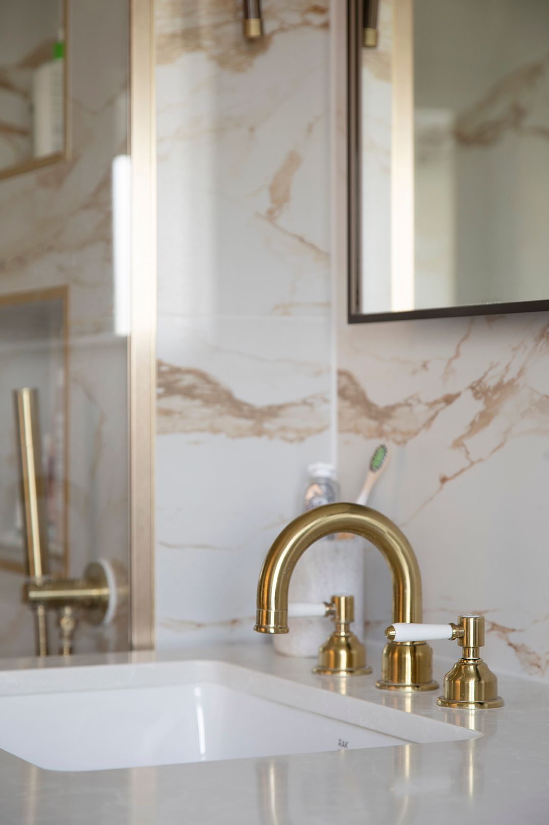 Brass three-hole basin taps detail on white countertop in Hertford luxury ensuite by Elisa Design