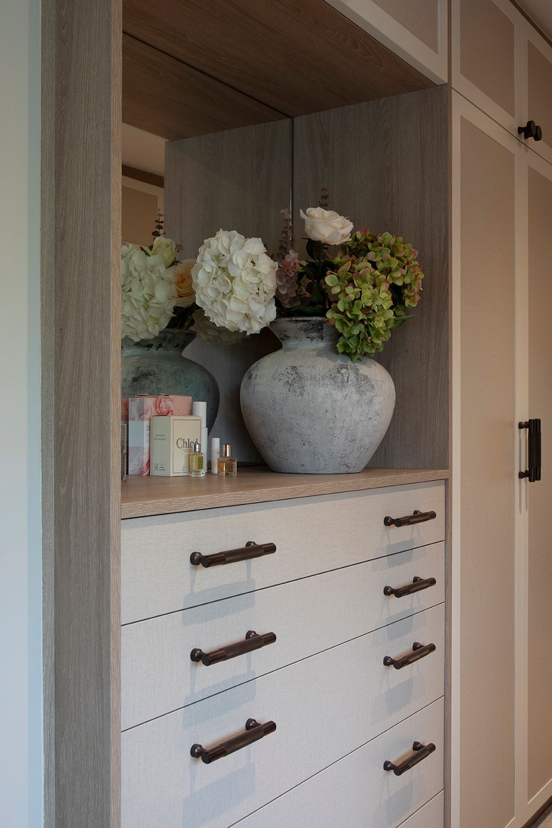 Custom wardrobe interior with LED-lit oak shelving, styled vases, and brass knurled handles - Elisa Design bespoke joinery