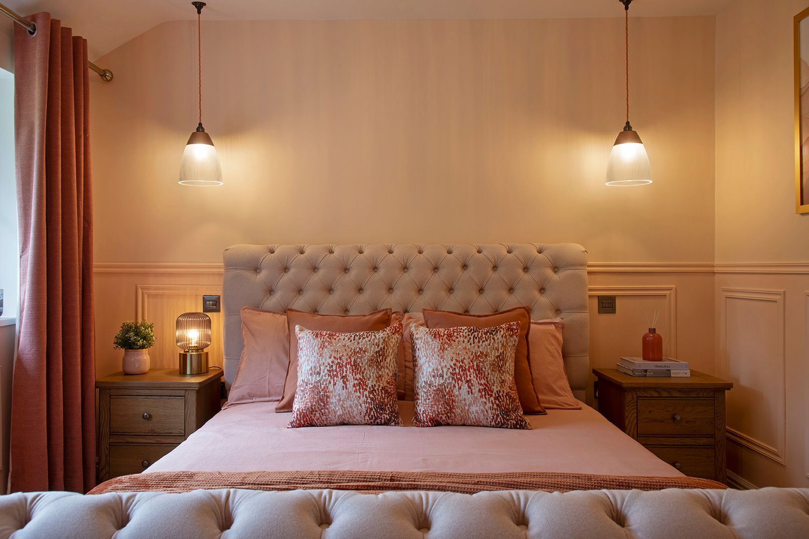 Elegant master bedroom with tufted headboard, symmetrical brass pendants, and soft peach wall panelling - Elisa Design