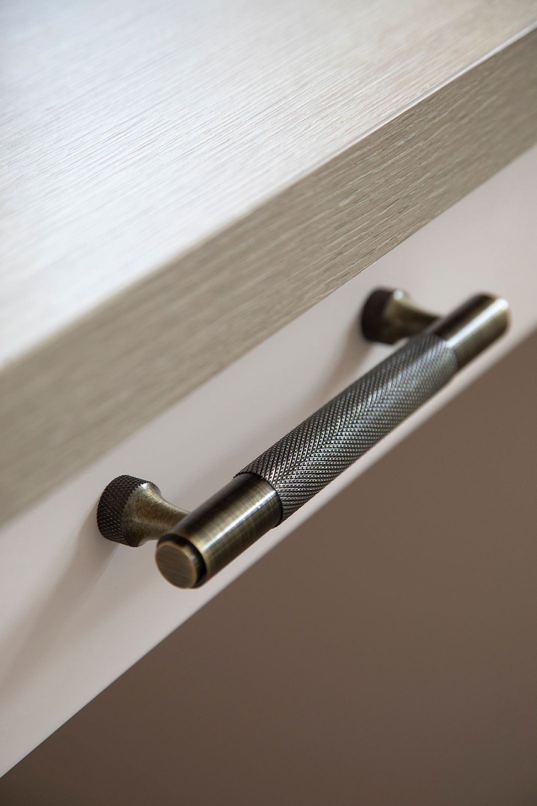 Close-up of Carlisle Brass knurled cupboard handle in antique brass on custom oak desk joinery - Elisa Design