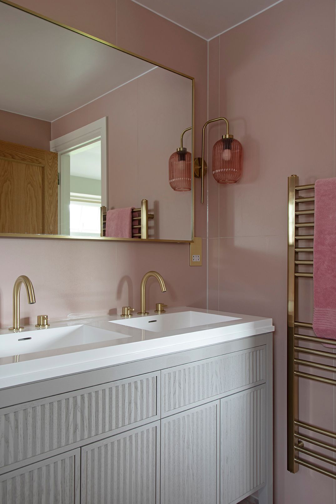 Pink ribbed glass wall sconce with brass detail and LED-lit mirror in luxury bathroom - Elisa Design interior design