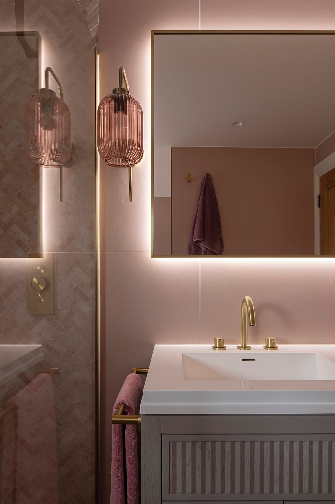 Bathroom vanity with pink ribbed glass sconces, LED-lit mirror, and brass fixtures - Elisa Design Welwyn Garden City