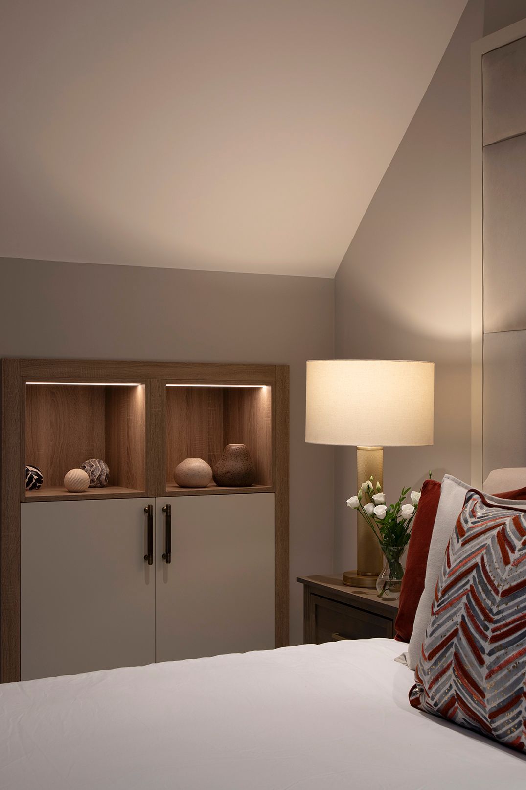 Bespoke storage unit with LED-lit display niches and brass handles in Bushey loft bedroom by Elisa Design