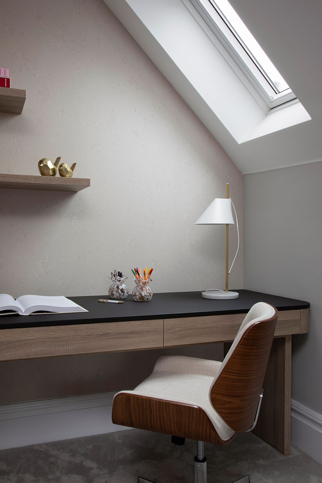 Loft workspace with floating desk, brass task lamp, and natural light from skylight in Bushey loft conversion
