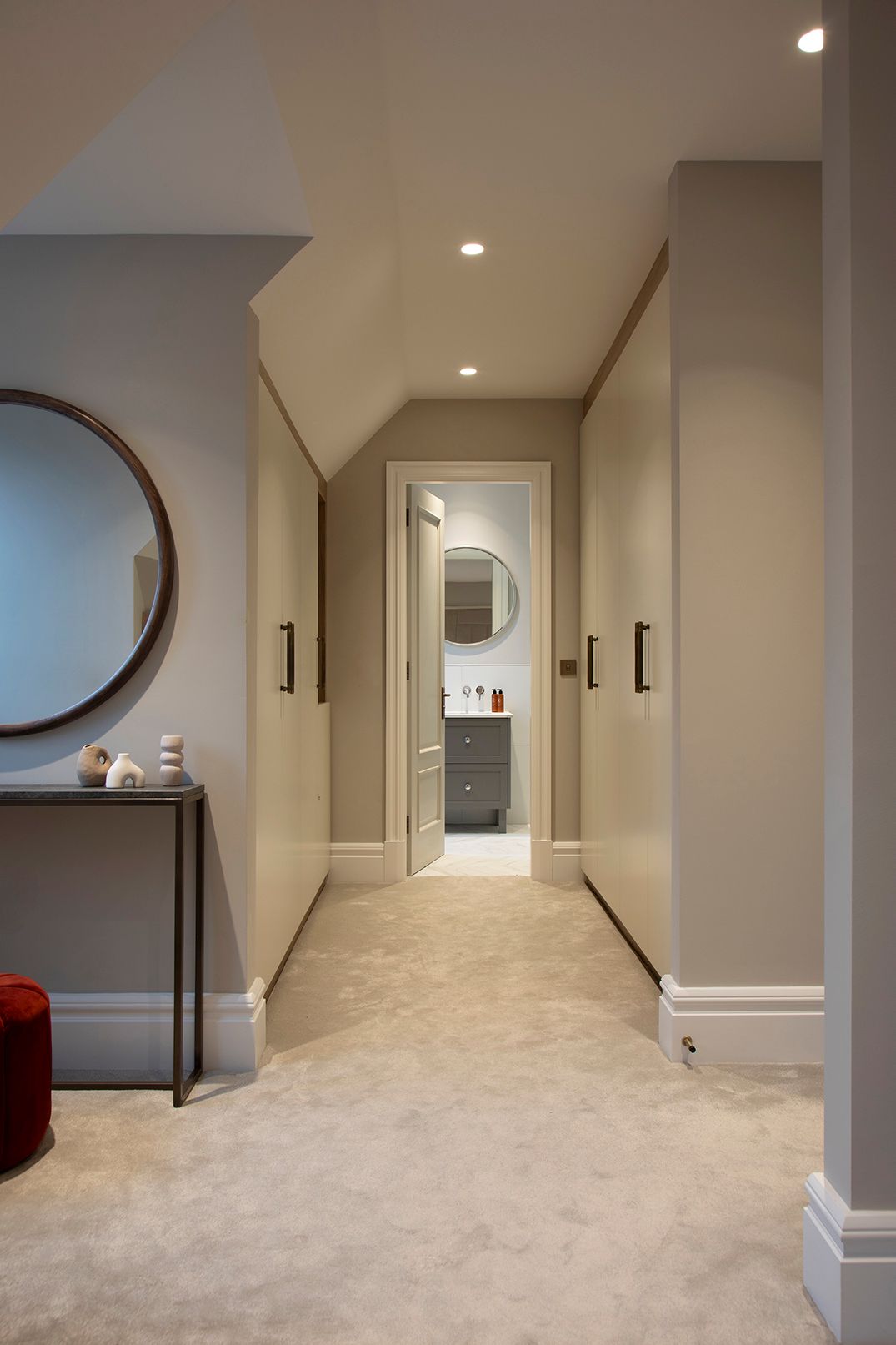 Elegant loft hallway with neutral palette, round mirror, and layered lighting in Bushey loft suite by Elisa Design