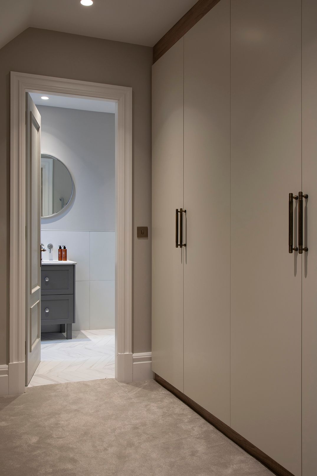Bespoke cream wardrobes with bronze handles and view to ensuite in Bushey loft conversion by Elisa Design