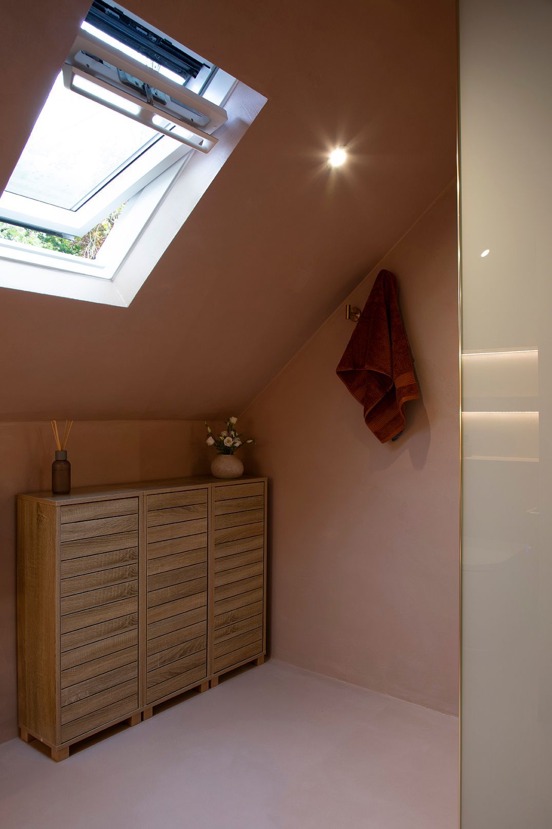 Loft bathroom corner in Watford with oak-effect cabinet, terracotta towel, and soft pink plaster walls designed