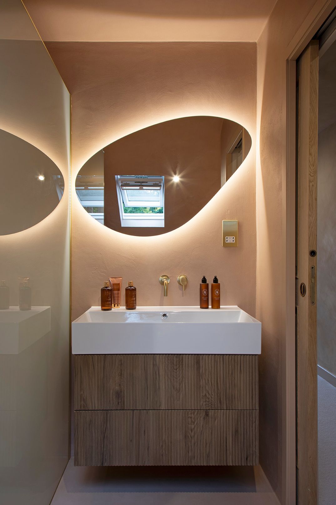 Spa-inspired ensuite with LED-backlit mirror, full microcement walls, and brass fixtures in Watford loft