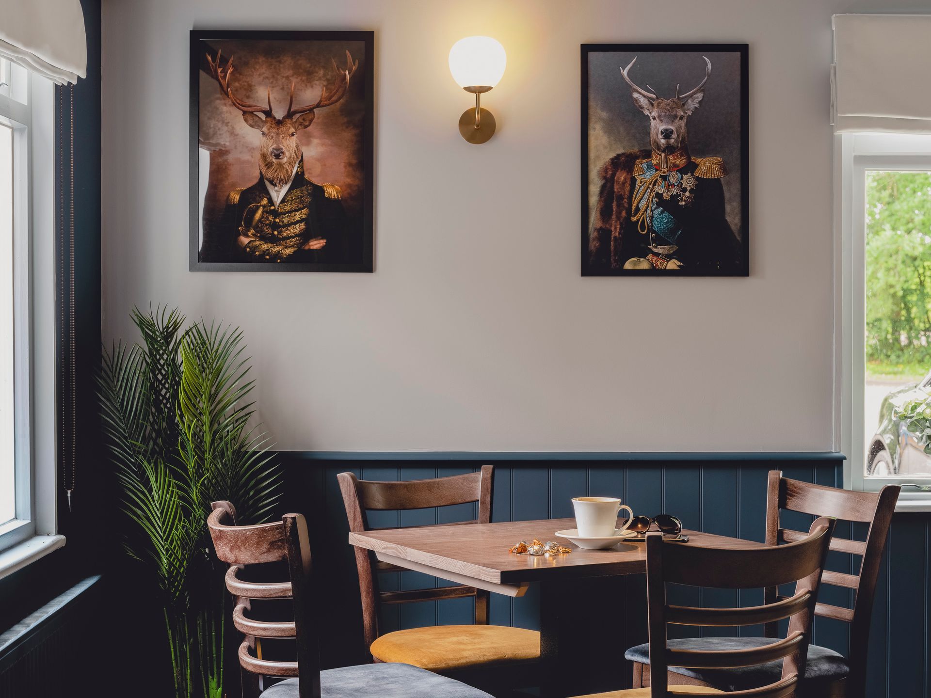 Cosy clubhouse corner with timber table, blue panelling and quirky stag portraits with a brass wall light.