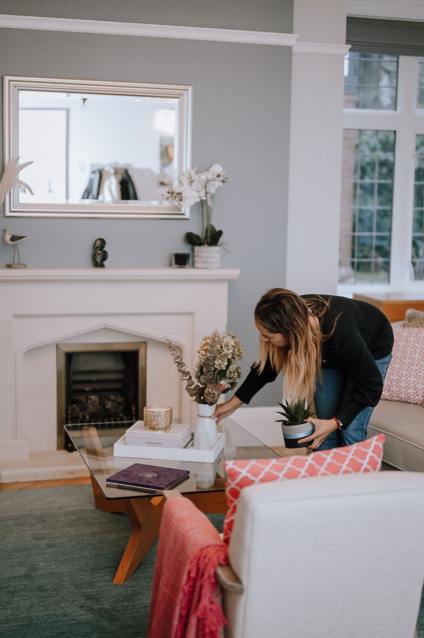 Designer styling the Principal’s office fireplace with books, vases and plants against soft grey walls.