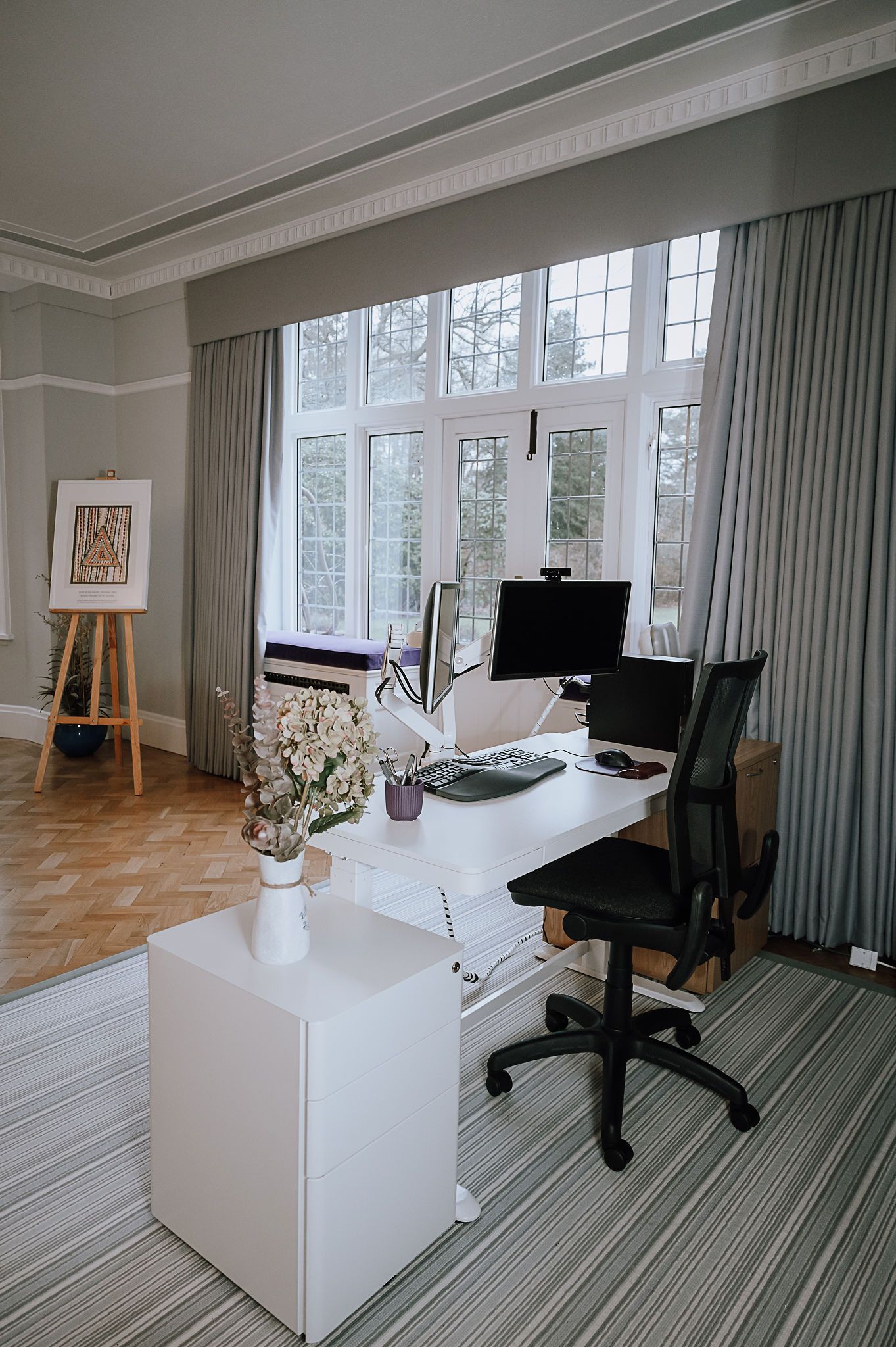 Principal’s white desk positioned by tall windows with dual screens, grey curtains and patterned rug.
