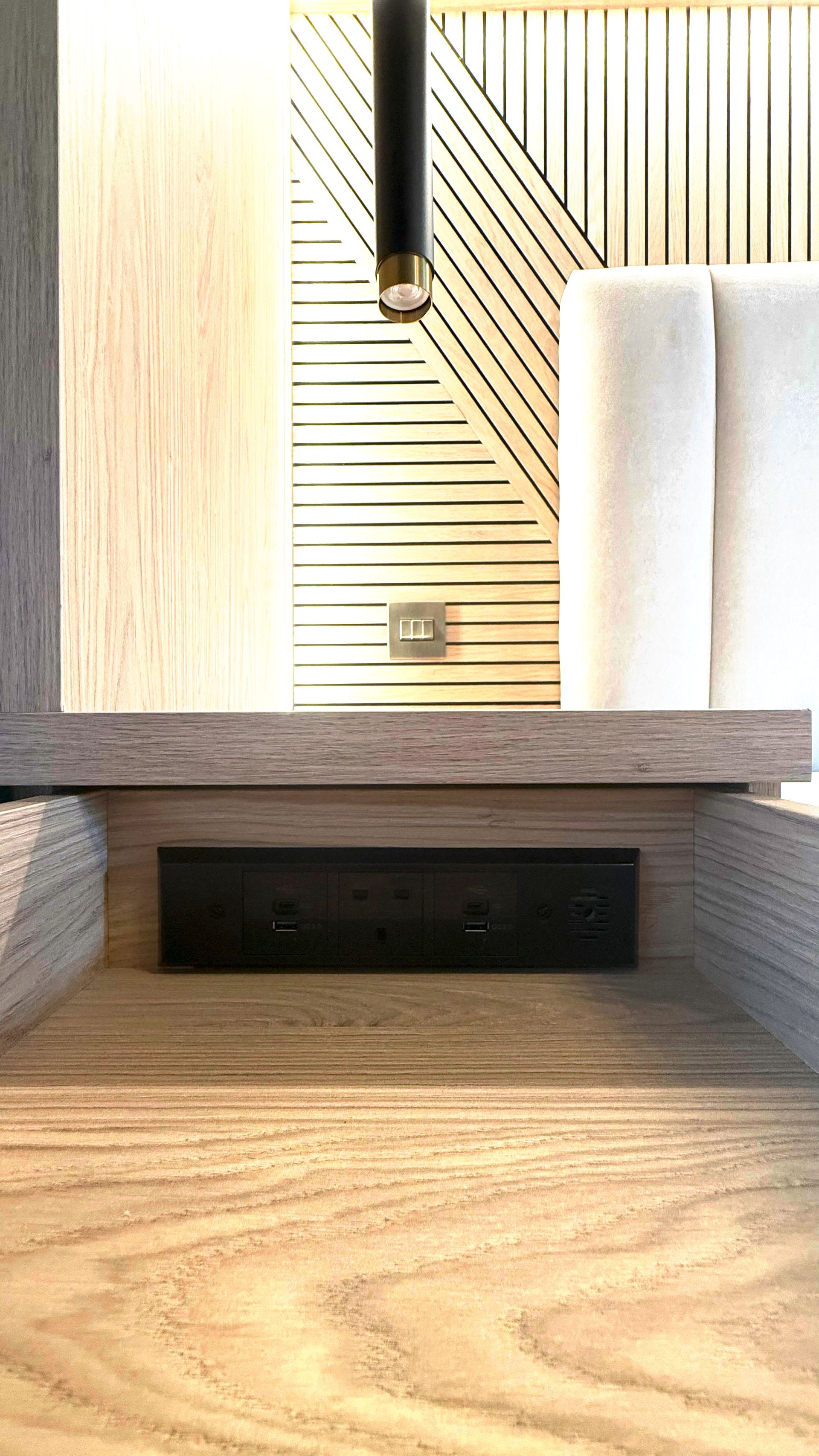 Close‑up of slatted timber headboard with integrated black downlight and upholstered bed in The Welwyn Family Edit.