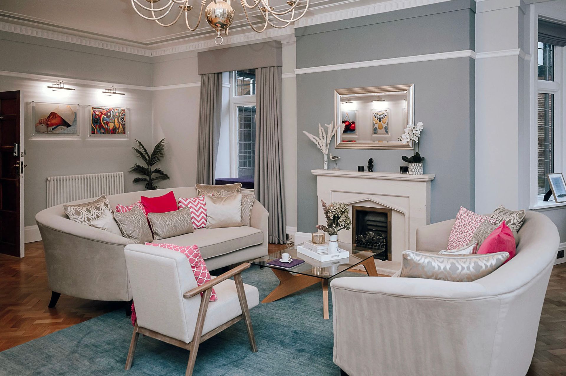 Principal’s office seating area with cream sofas, fireplace, picture lights and hot pink accents on cushions and throw.