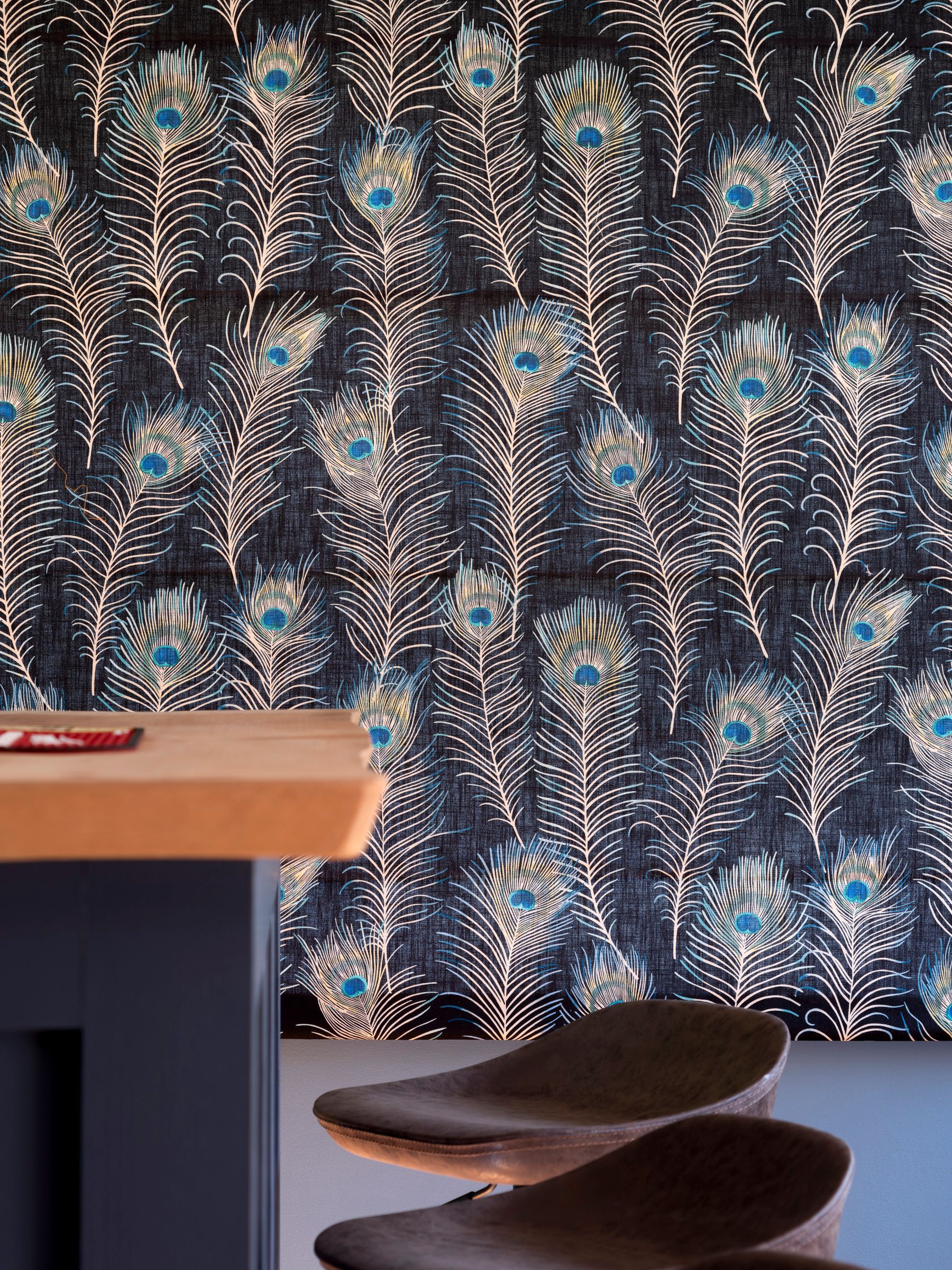 Detail of peacock‑feather fabric behind blue bar with leather stools in Knebworth games room.