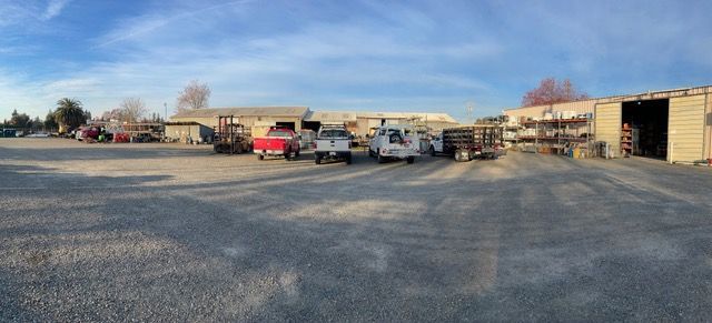 a row of trucks are parked in a gravel lot in front of a building .