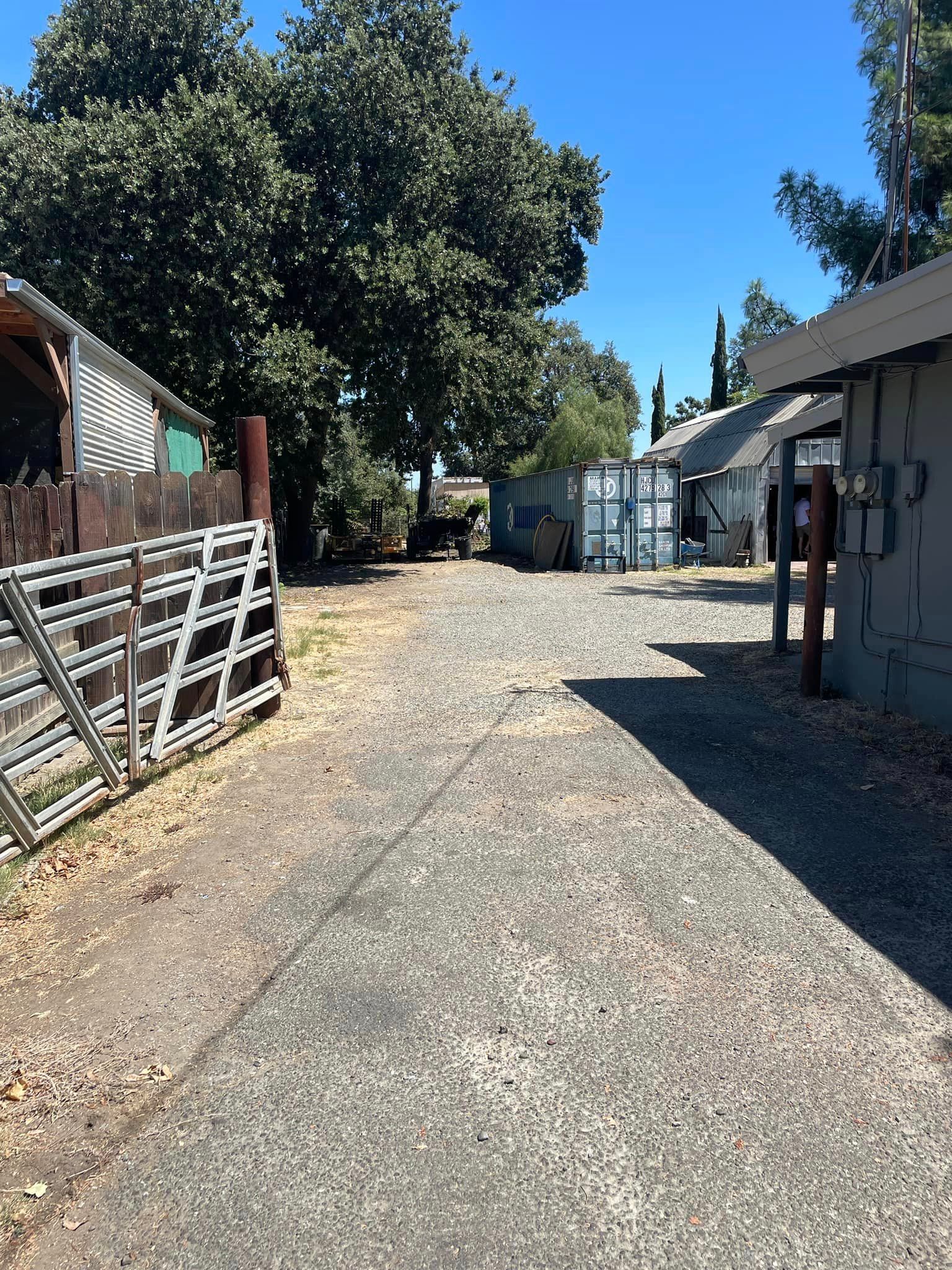 A gravel road leading to a fenced in area with buildings and trees.